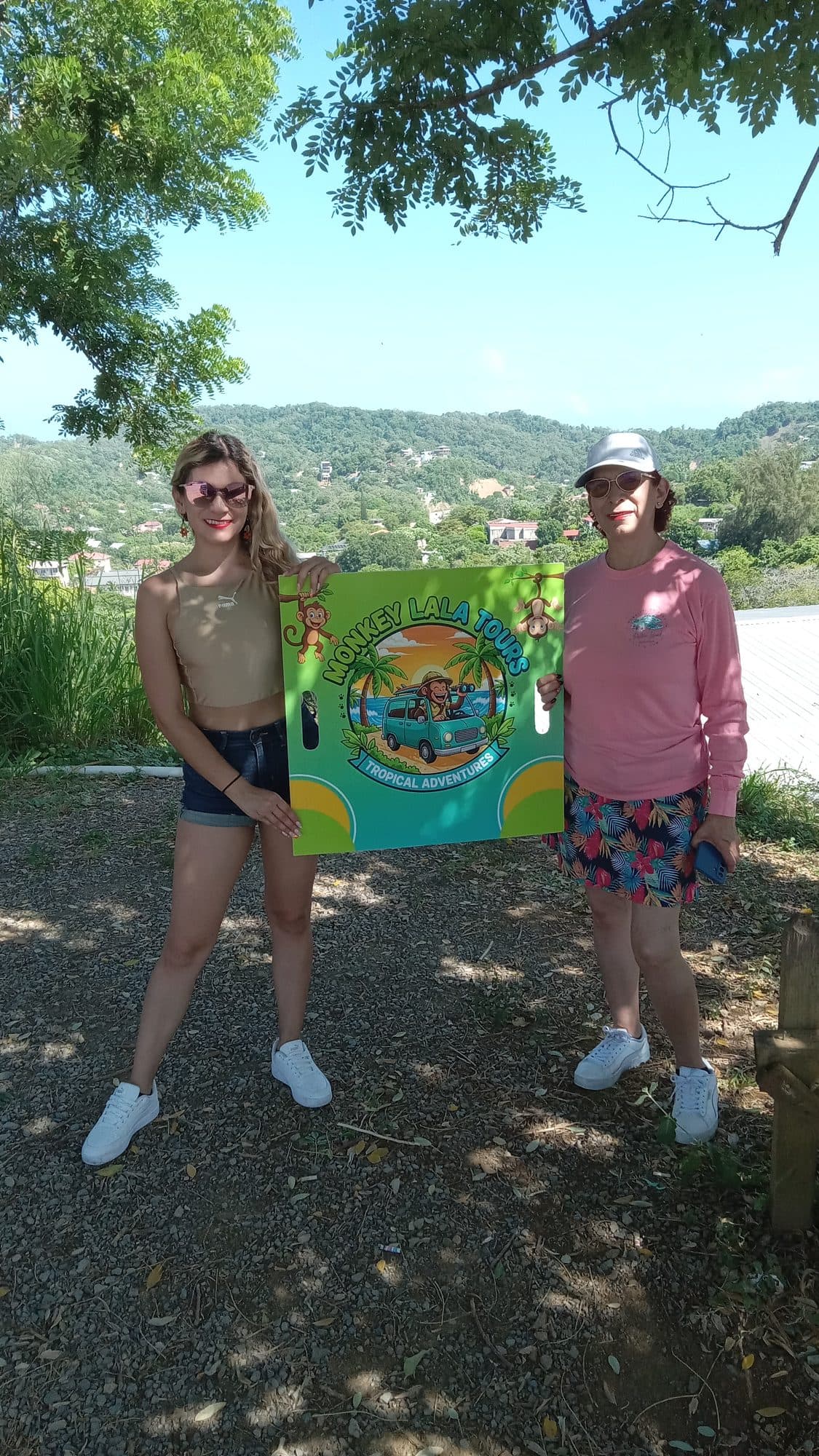 Two Monkey Lala guides holding the painted company sign at the meeting point, with the hillside behind them